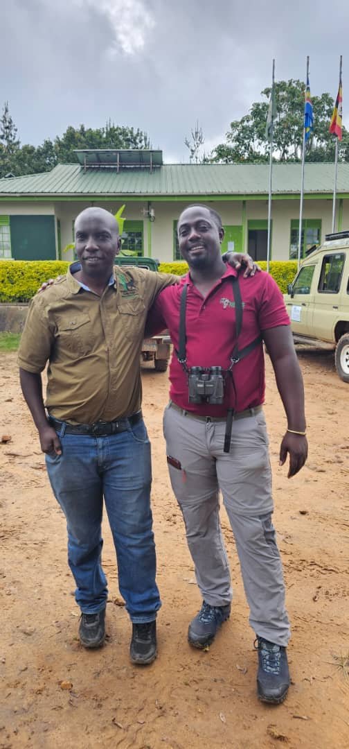 Safari guide in red shirt with binoculars, safari vehicle in background, Uganda