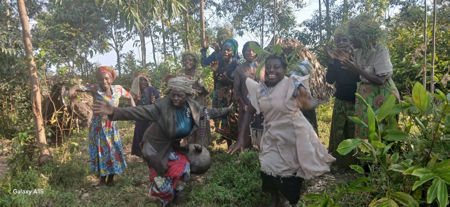 Batwa women dancing and clapping among trees during a community visit in Nkuringo